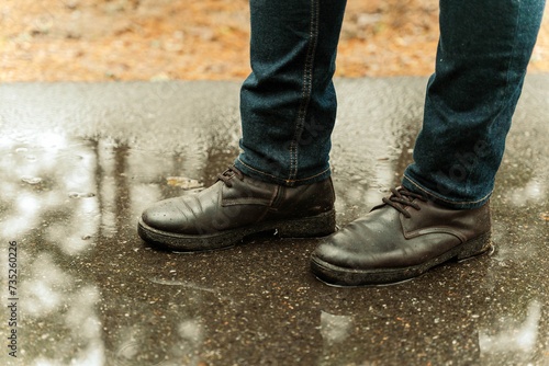 female legs in jeans and black boots standing on wet asphalt in rain