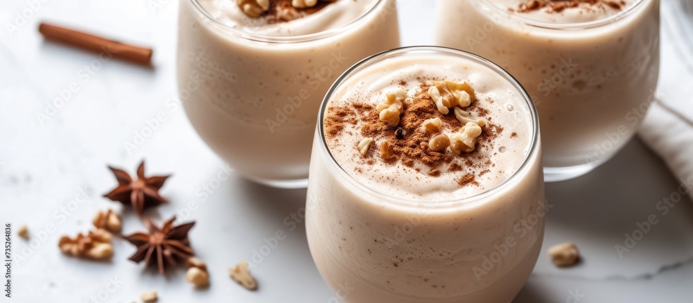 Two glasses of creamy eggnoi topped with crunchy nuts and aromatic cinnamon in elegant setting for festive celebration Two glasses of creamy eggnoi topped with crunchy nuts and aromatic cinnamon in elegant setting for festive celebration