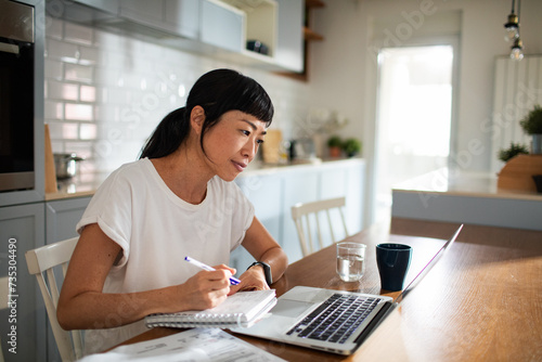 Worried woman holding papers and using laptop at home photo