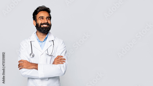Cheerful indian bearded doctor looking away with folded arms photo