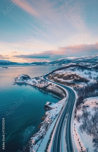 an aerial view of a road next to a body of water with snow on the ground and mountains in the background. photo
