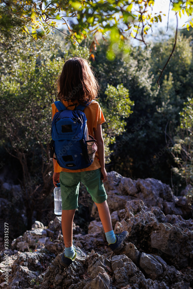 Obraz premium A boy with a backpack and a bottle of water walks through the forest, a child explores the wild.