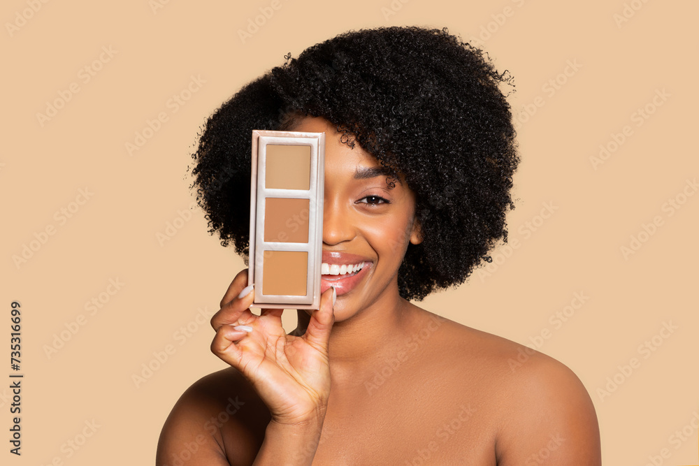 Happy young black woman holding concealer palette near face - obrazy, fototapety, plakaty 