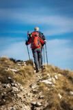 Two hikers walk on the mountain path, helping themselves up the climb with trekking poles.