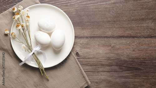 Easter table setting with white eggs and dried flowers on wooden background.