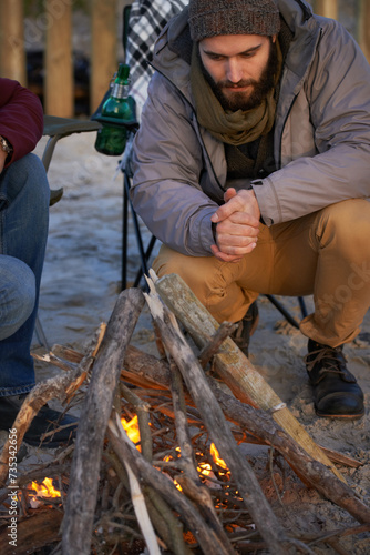 Campfire, wood and men by beach for travel on vacation, adventure or holiday camping. Nature, outdoor and young male people sitting on chair in sand with flame for heat on weekend trip in winter.