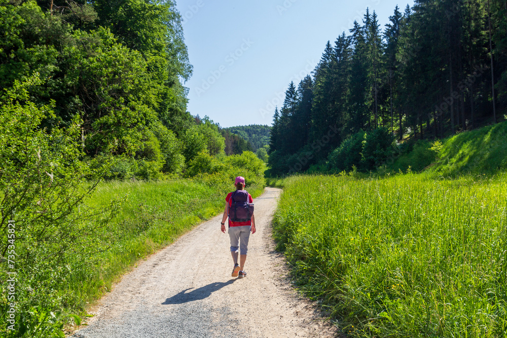Woman hiking on path with hill panorama and forest with trees near Obertrubach in Franconian Switzerland, Germany