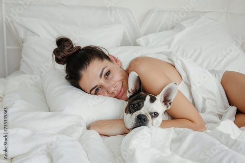 A woman finds comfort and peace as she lays in bed with her beloved dog, both nestled under a cozy white blanket in the indoor space of their home
