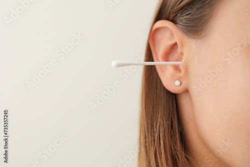 Cropped shot of unrecognisable young woman with cotton swab in ear isolated on white background. Close up female uses hygienic stick for cleaning ear. Daily habit routine. Hygiene and health care.