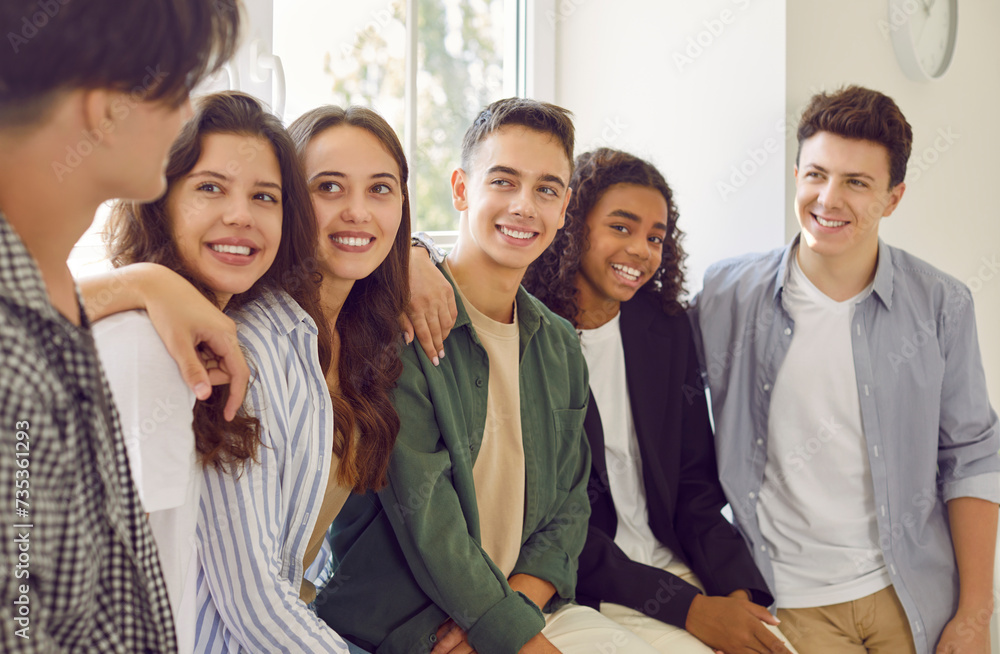Portrait of a happy cheerful high school students in casual clothes standing together in hallway and friendly smiling to each other. Joyful diverse friends guys and girls talking indoors. Portrait of a happy cheerful high school students in casual clothes standing together in hallway and friendly smiling to each other. Joyful diverse friends guys and girls talking indoors.