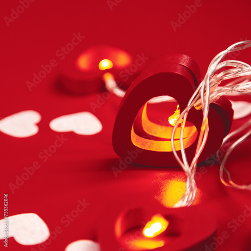 Holiday design concept background with garlands of hearts and paper hearts on red table background.
