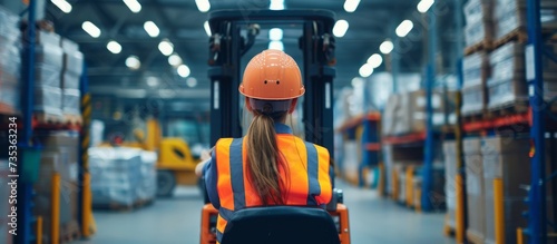 Confident female worker in hard hat and safety vest operating a forklift in industrial warehouse photo