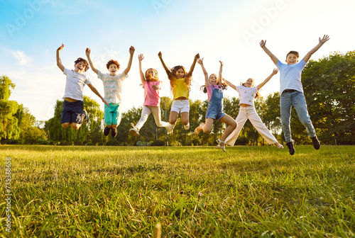 Children friends having fun on summer vacation. Overjoyed kids playing in park. Group of cheerful boys and girls feeling free and happy and jumping on green grass up to clear blue sky. Low angle shot