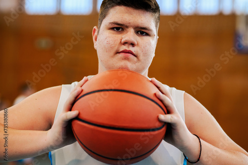 Close up of a teenage basketball player posing with a ball on court.