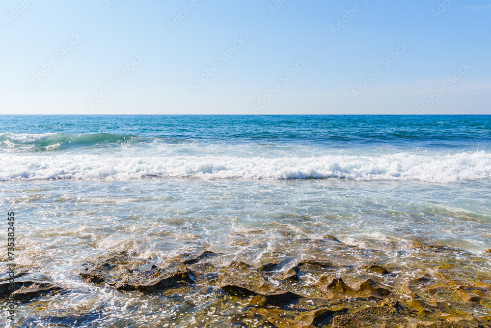 Enchanting Calm Blue Ocean Waves Hitting and Splashing on the Seashore and Beach Under the Clear Sky, During a Hot Sunny Summer Day Morning 