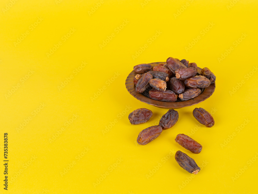 Obraz premium Heap of date fruits, side view isolated studio image heap of date fruits. Isolated yellow background, copy space. Vintage, classic copper bow. Ramadan month concept idea photo.