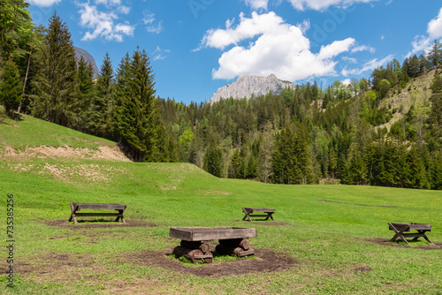 Wooden feed troughs on lush green alpine meadow with panoramic view of mountain peak Foelzstein and Foelzkogel in Hochschwab massif, Styria, Austria, Hiking trail in remote Austrian Alps in summer photo
