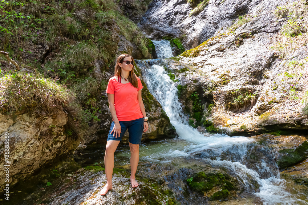 Naklejka premium Hiker woman next to idyllic river Foelzbach, Hochschwab mountains, Styria, Austria. Hiking trail in alpine forest. Remote Austrian Alps in summer. Sense of escapism, reflection. Connect with nature