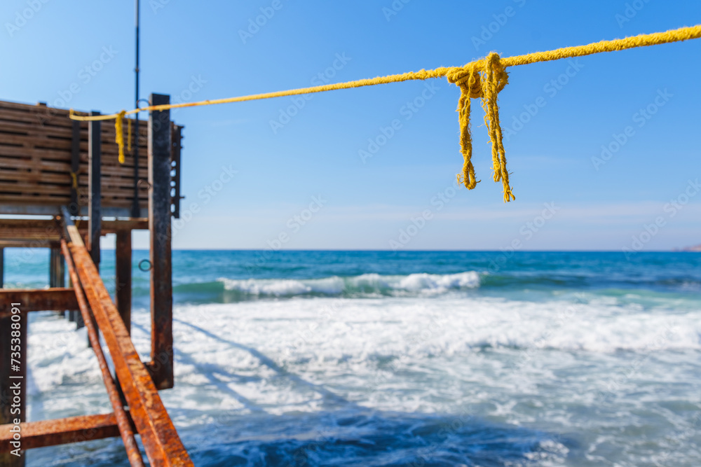 Obraz premium Rope String knot Hanging on a Wooden Boardwalk Bay at a Sandy Beach Infront of the Blue Sea and Sky