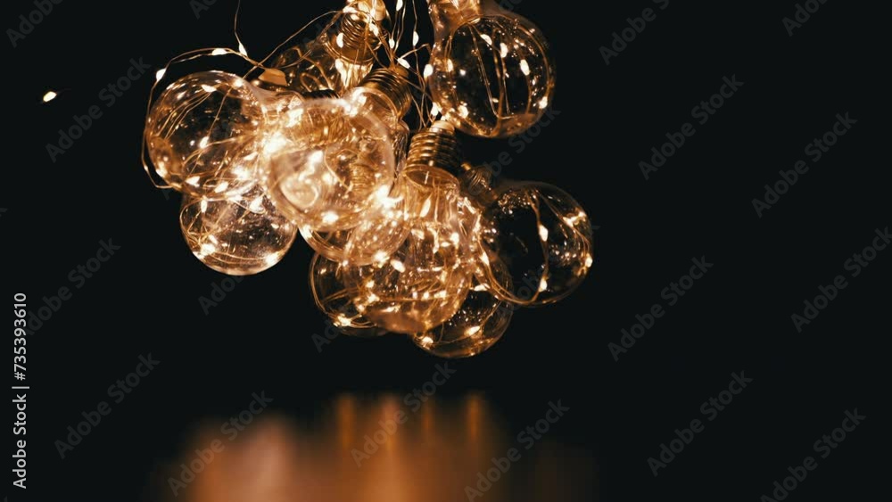 Bunch of Glowing Garland of Glass Light Bulbs with Dim Yellow Light in a Dark Room. Close up. Texture. Christmas decorations with retro style hanging electric lights illuminating the space. Design. Bunch of Glowing Garland of Glass Light Bulbs with Dim Yellow Light in a Dark Room. Close up. Texture. Christmas decorations with retro style hanging electric lights illuminating the space. Design.