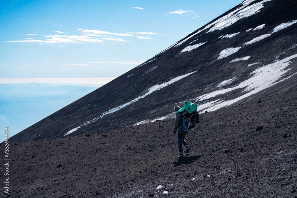 Man with big backpack going down from volcano
