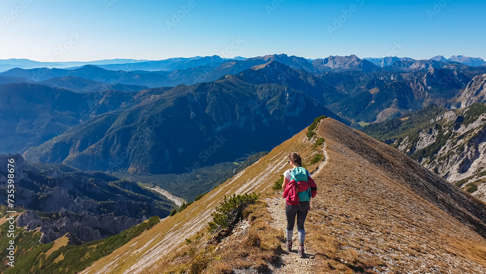 Hiker woman on idyllic hiking trail on alpine meadow with scenic view of majestic Hochschwab mountain range, Styria, Austria. Wanderlust in remote Austrian Alps. Sense of escapism, peace, reflection - obrazy, fototapety, plakaty 