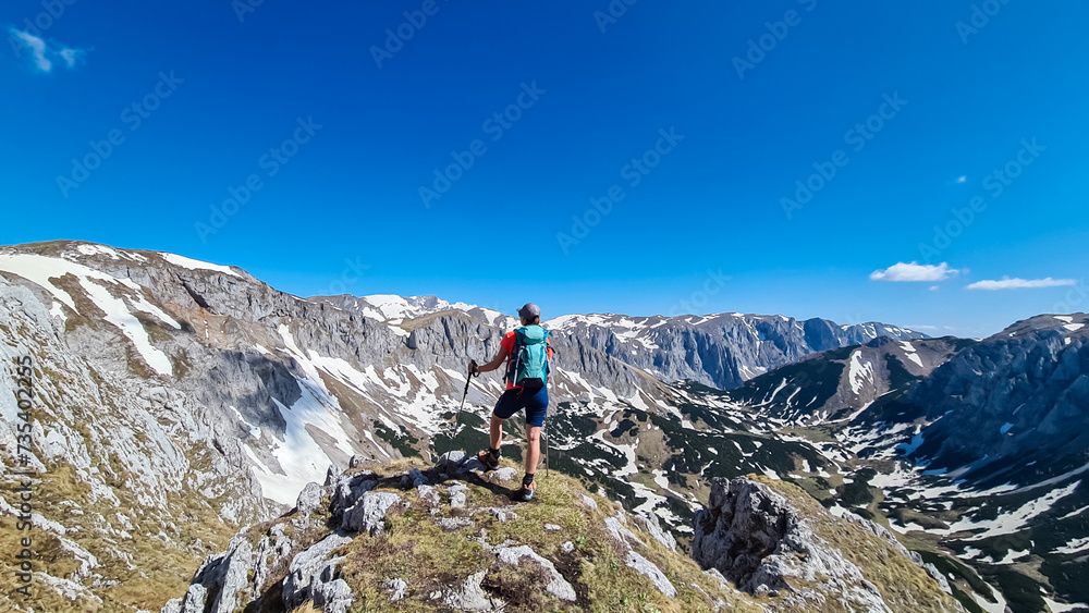 Naklejka premium Hiker woman with panoramic view of majestic mountain peak Ringkamp in wild Hochschwab massif, Styria, Austria. Scenic hiking trail in remote Austrian Alps on sunny day. Wanderlust in alpine spring