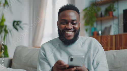 Smiling bearded African man working at home while sitting on the sofa.Concept of young people using mobile devices.Blurred background.Cropped