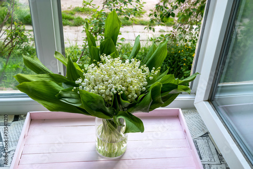 Spring bouquet of lilies of the valley in interior of apartment. Bouquet of lilies of the valley on sill of an open window