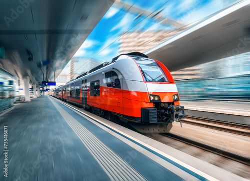 High speed train in motion on the train station at sunset in Vienna, Austria. Red modern intercity passenger train with motion blur effect. Railway platform. Railroad. Commercial transportation