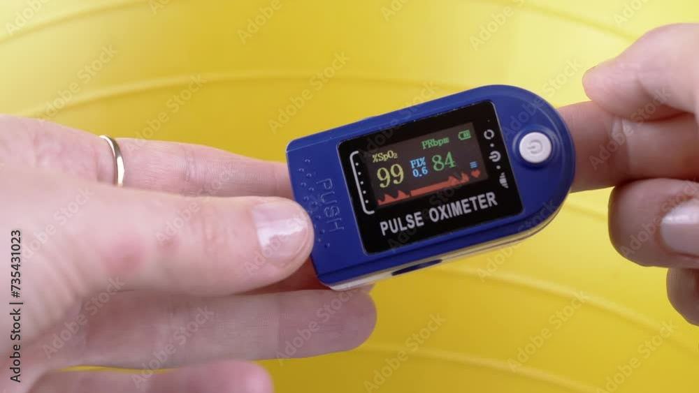 Hands Measure Pulse and Oxygen Saturation Using a Pulse Oximeter During Exercise. Close up. Dial with sensors and indicators on the device. Measurement of heart rate. Yellow background. Fitness ball. Hands Measure Pulse and Oxygen Saturation Using a Pulse Oximeter During Exercise. Close up. Dial with sensors and indicators on the device. Measurement of heart rate. Yellow background. Fitness ball.