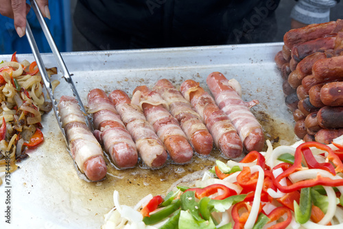 Street vendor cooking bacon wrapped hot dogs, tongs turning food. Popular cuisine for street fairs and events