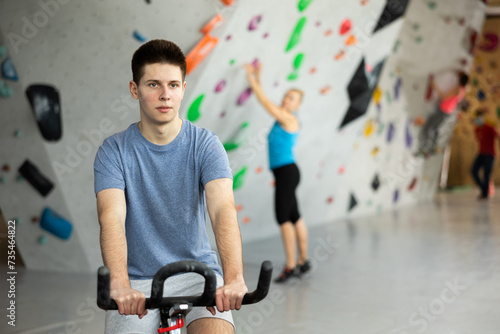 Young man riding exercise bike to warm-up before training in bouldering center.