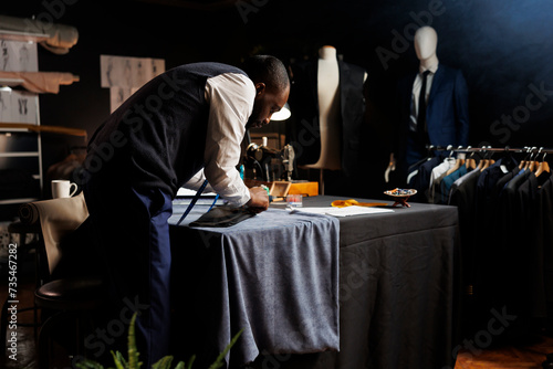Meticulous suitmaker focused on perfecting client comissioned exquisite suit blazer for upcoming wedding. Couturer working on bespoke sartorial attire in professional tailoring shop photo