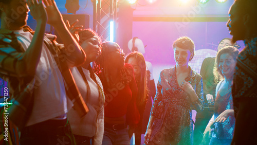Young adults having fun dancing at party, enjoying breakdance battle with group of friends on dance floor. People showing off dance moves and jumping around in discotheque, nightlife.