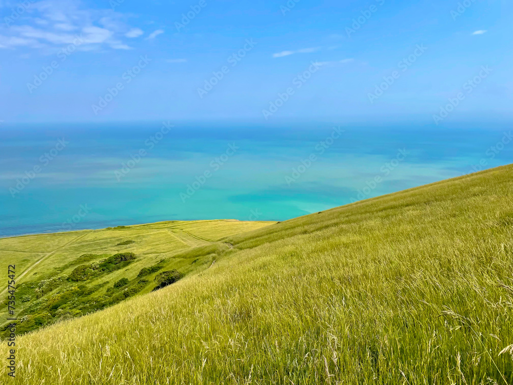 A stunning hilly coastline covered with green grass above the turquoise blue sea