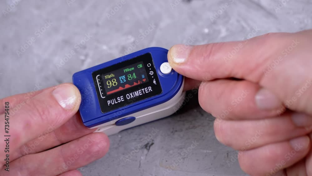 Woman Measures Pulse and Oxygen Saturation Using a Pulse Oximeter at Home. Close-up. Concrete background. A dial with sensors and indicators on the device. Measurement of heart rate, pulse, heartbeat. Woman Measures Pulse and Oxygen Saturation Using a Pulse Oximeter at Home. Close-up. Concrete background. A dial with sensors and indicators on the device. Measurement of heart rate, pulse, heartbeat.