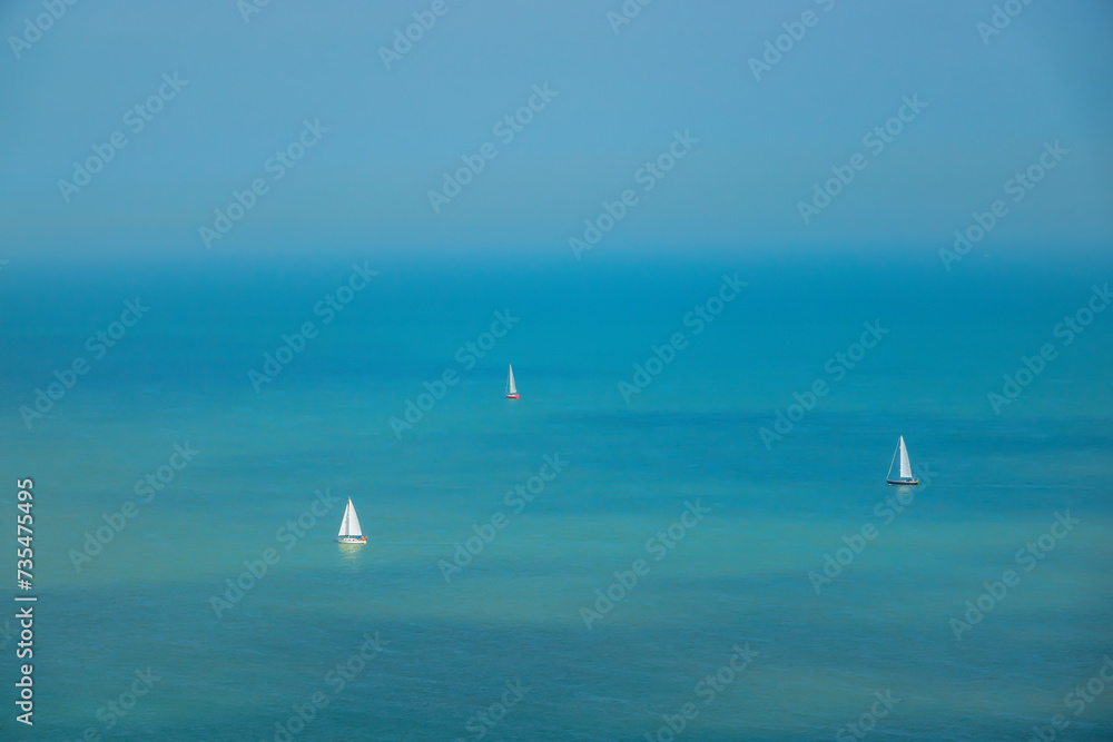 Obraz premium Sunny summer day with sailboats sailing on the turquoise blue ocean around cape