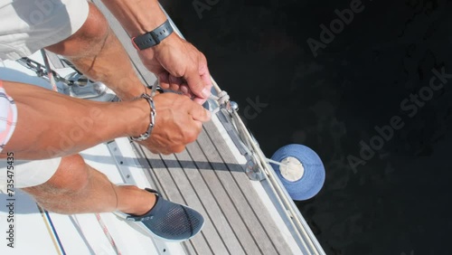 Seasoned yachtsman unties mooring ball preparing vessel for docking. Sailor engages in mooring process for secure stay in harbor