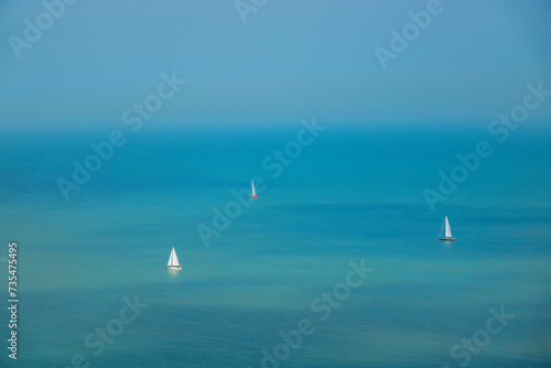Sunny summer day with sailboats sailing on the turquoise blue ocean around cape