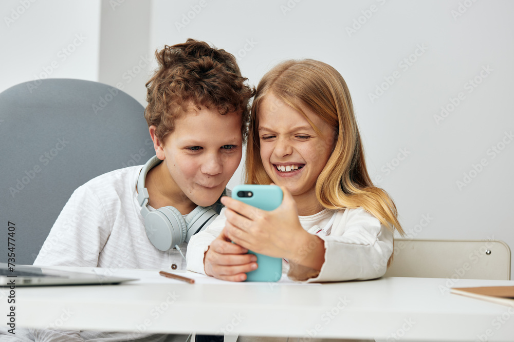 Happy Caucasian school children sitting at home on the living room table, engrossed in their laptops and tablets The boy and girl are engaged in online learning, wearing headphones and typing on their Happy Caucasian school children sitting at home on the living room table, engrossed in their laptops and tablets The boy and girl are engaged in online learning, wearing headphones and typing on their