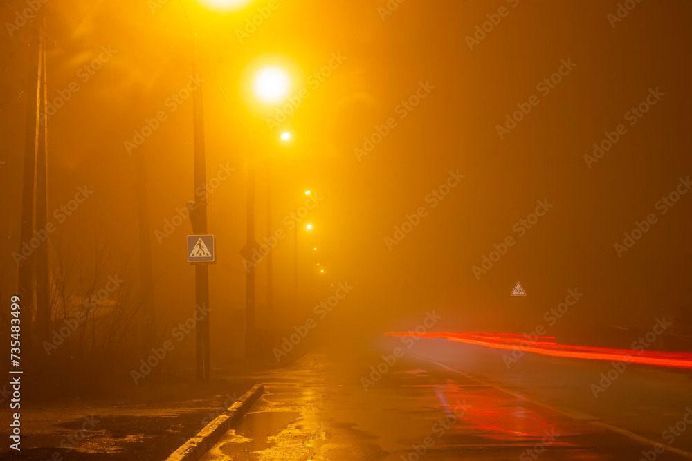 Orange street lights in heavy fog and cars drive by. Long exposure, blurred cars and light lines from car headlights
