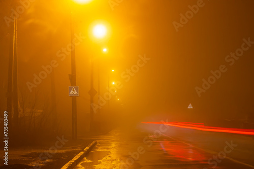 Orange street lights in heavy fog and cars drive by. Long exposure, blurred cars and light lines from car headlights © Vladyslav Sydorenko