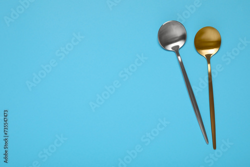 Shiny spoons on light blue background, top view. Space for text