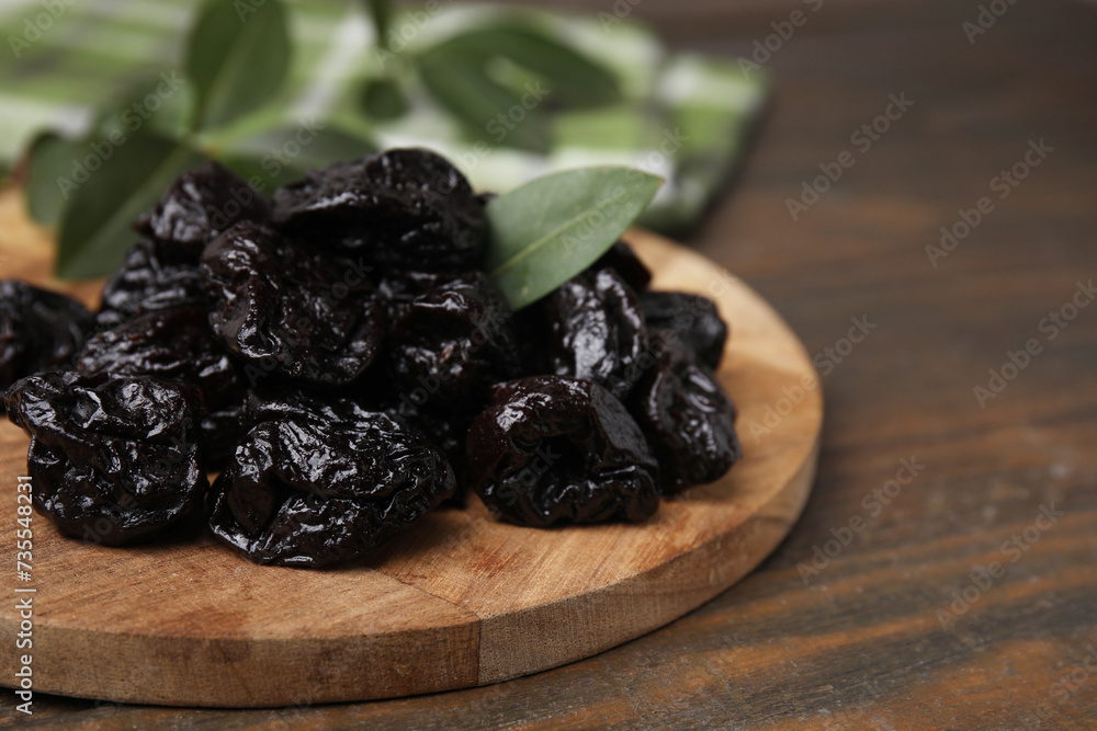 Tasty dried prunes and green leaf on wooden table, closeup Tasty dried prunes and green leaf on wooden table, closeup
