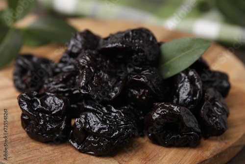 Tasty dried prunes and green leaf on wooden board, closeup