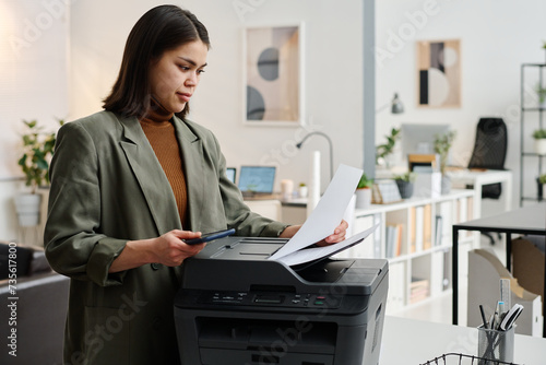 Medium shot of young woman wearing smart casual outfit working in modern office printing documents photo