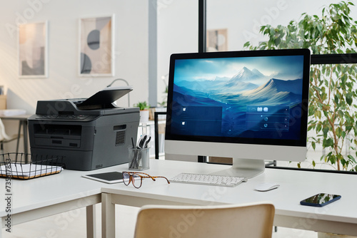 No people shot of modern desktop computer and printer on desk in modern office interior, copy space photo
