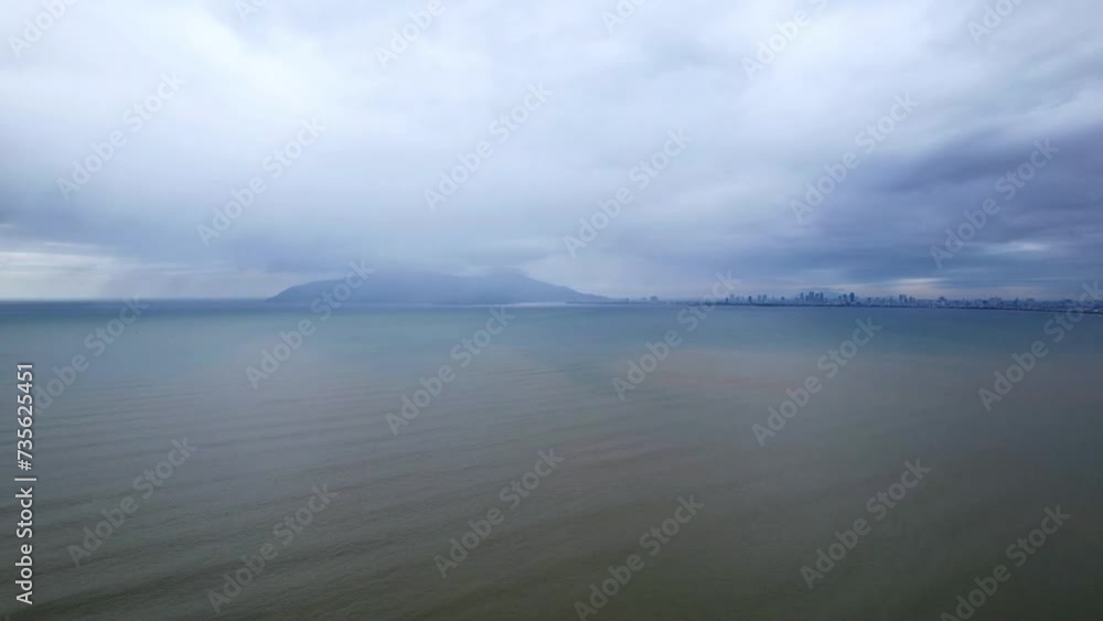 Overcast seascape with a distant city skyline and mountains, depicting calm before a storm or serene solitude, suitable for weather-related or reflective thematic video content Overcast seascape with a distant city skyline and mountains, depicting calm before a storm or serene solitude, suitable for weather-related or reflective thematic video content