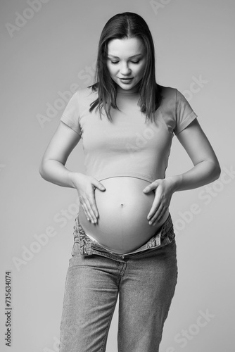 Black and white portrait of young pretty pregnant woman on gray background.